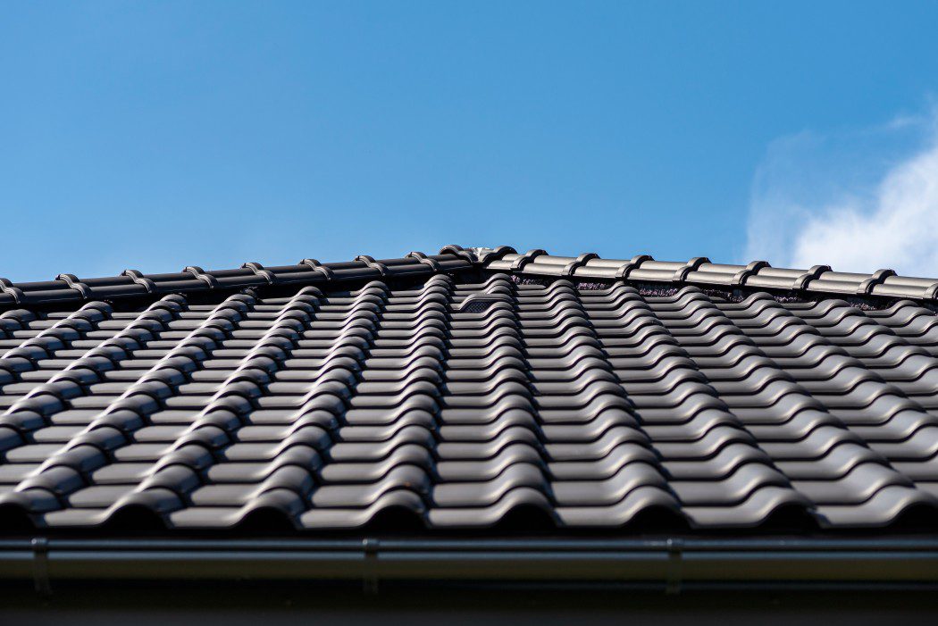 black glazed ceramic roof tiles with a blue sky in the background. How to fix a leaking roof.