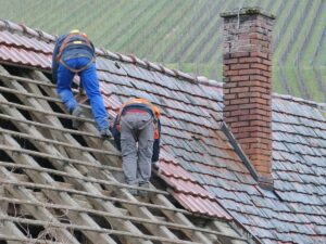 two roofers working to repair a tile roof from old blue tiles to new red tiles of an old house in Arizona